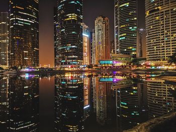 Illuminated modern buildings in city against sky at night