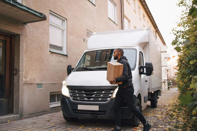 Side view of man carrying box while walking by delivery van in city