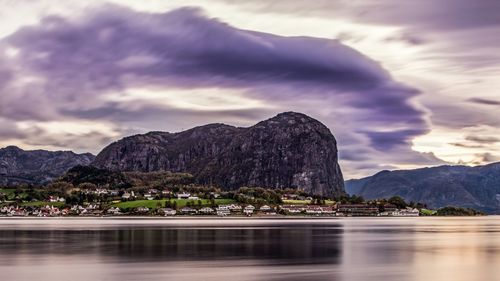 Calm lake in front of mountains against cloudy sky