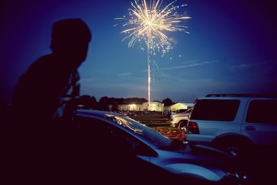 Rear view of man looking at illuminated fireworks against sky at dusk