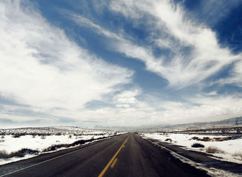 Road leading towards snowcapped mountains against sky