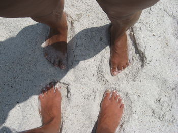 Low section of friends standing on sand at beach