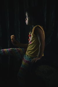 Side view of girl eating food while sitting in darkroom at home