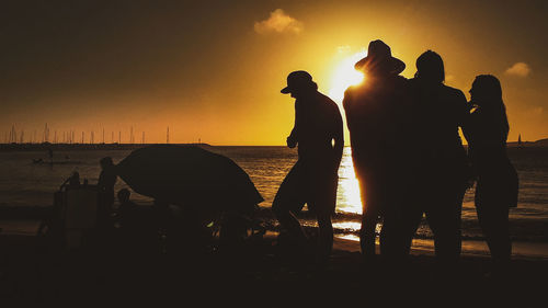 Silhouette people on beach against sky during sunset