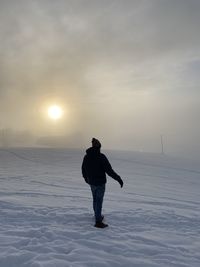 Full length of man standing on snow covered field against sky during sunset