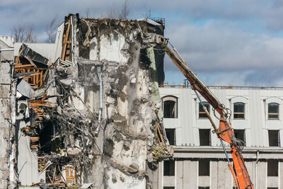 Excavator with long mechanical arm at height breaks off pieces of the house. 