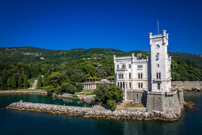 Buildings by river against clear blue sky