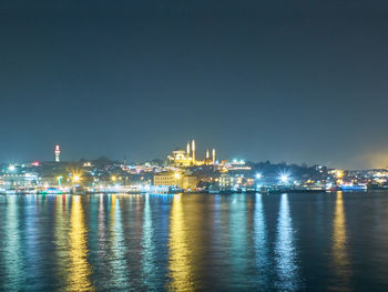 Illuminated city by sea against clear sky at night