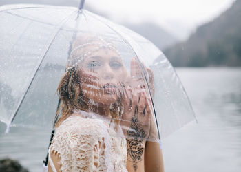 Beautiful young woman bride in a boho dress and with an umbrella stands in the rain in nature