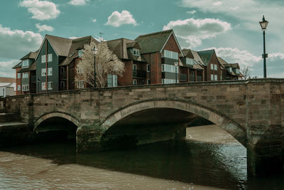 Arch bridge over river amidst buildings against sky