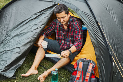 Man relaxing in tent at camping during summer vacation. planning next trip. concept of camp life