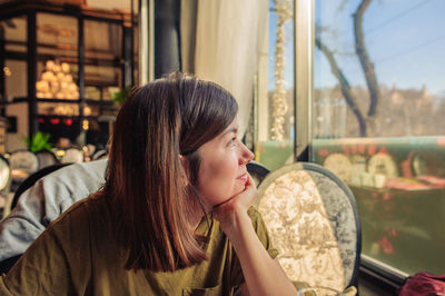 A beautiful young girl sits in a restaurant and looks out the window