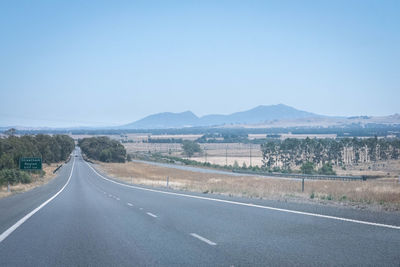 Empty road by landscape against clear sky