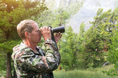 Side view of man looking through binoculars in forest