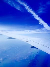 Aerial view of aircraft wing over landscape against blue sky