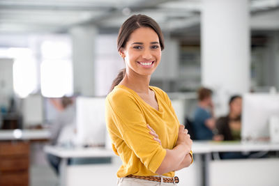Portrait of smiling businesswoman standing with arms crossed at office
