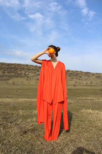 Full length of woman holding fruit while standing on field against sky