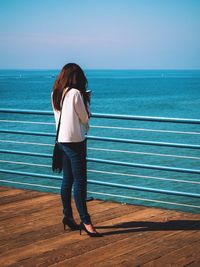 Rear view of woman standing on promenade by sea against sky