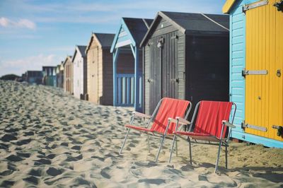 Empty chairs and huts at beach against sky