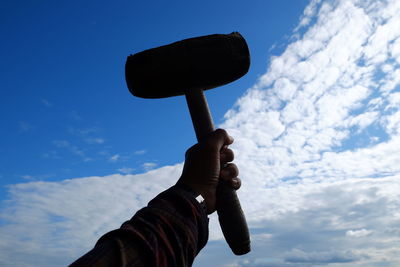 Low angle view of person holding wooden hammer against sky