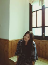 Young woman looking away while standing against wall