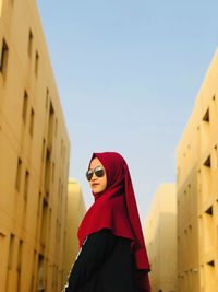 Low angle view of woman standing by building against clear sky