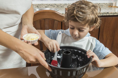 Midsection of mother preparing food with son at home