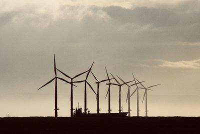 Silhouette wind turbines on land against sky at sunset