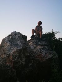 Low angle view of boy on rock against clear sky