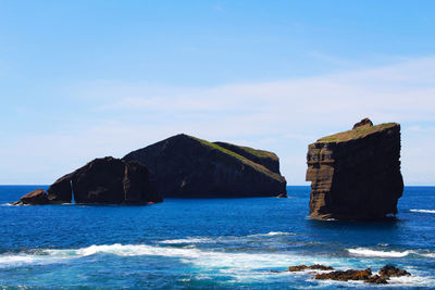 Built structure on rocks by sea against blue sky