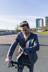 Mature businessman commuting in the city with his kick scooter, checking the time