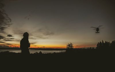 Silhouette man on horse at beach against sky at sunset