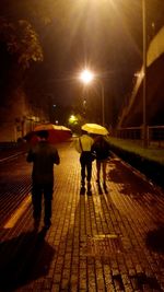 Rear view of man walking on illuminated street at night