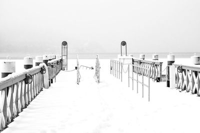 Wooden posts on snow covered pier against clear sky