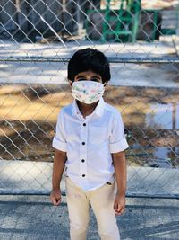 Portrait of boy standing by chainlink fence