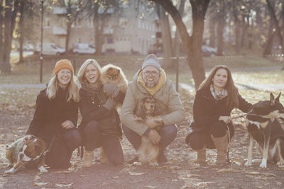 Portrait of happy man and women crouching with dogs at park during autumn