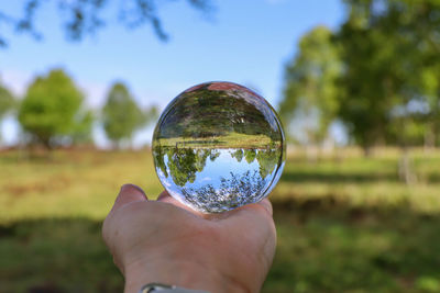 Cropped image of hand holding crystal ball on field