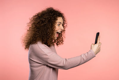 Midsection of woman using smart phone against pink background