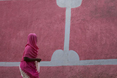 Side view of woman standing against pink wall