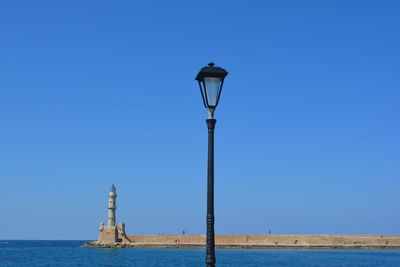 Street light by lighthouse against clear blue sky
