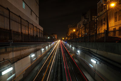 Light trails on illuminated street amidst buildings at night