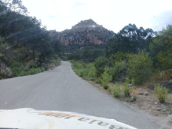 Road amidst trees and mountains against sky