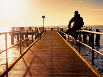 Alone man goes on the wooden pier in the sunrise. smooth water level