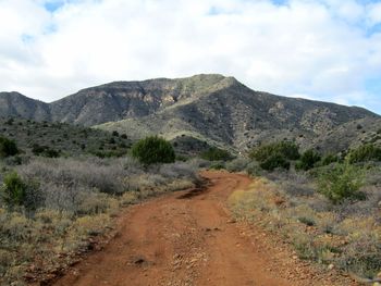 Dirt road leading towards mountains against sky