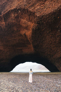 Rear view of woman standing on sand at beach by mountain