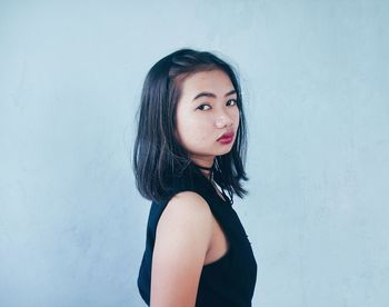 Portrait of young woman standing against wall