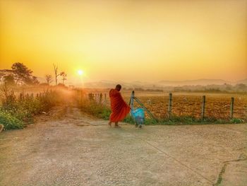 Rear view of monk walking on footpath against sky during sunset