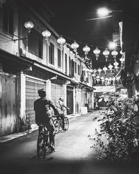 Rear view of man riding bicycle on street at night