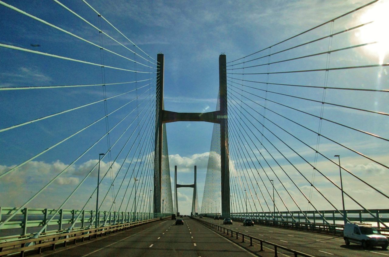 transportation, bridge, cable-stayed bridge, suspension bridge, sky, built structure, architecture, road, the way forward, motor vehicle, car, engineering, city, nature, mode of transportation, cable, travel, travel destinations, cloud, steel cable, street, land vehicle, diminishing perspective, highway, day, outdoors, line, traffic, vanishing point, tourism, water, building exterior, overpass, sunlight, blue, sign