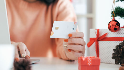 Midsection of woman holding credit card with christmas decoration on table